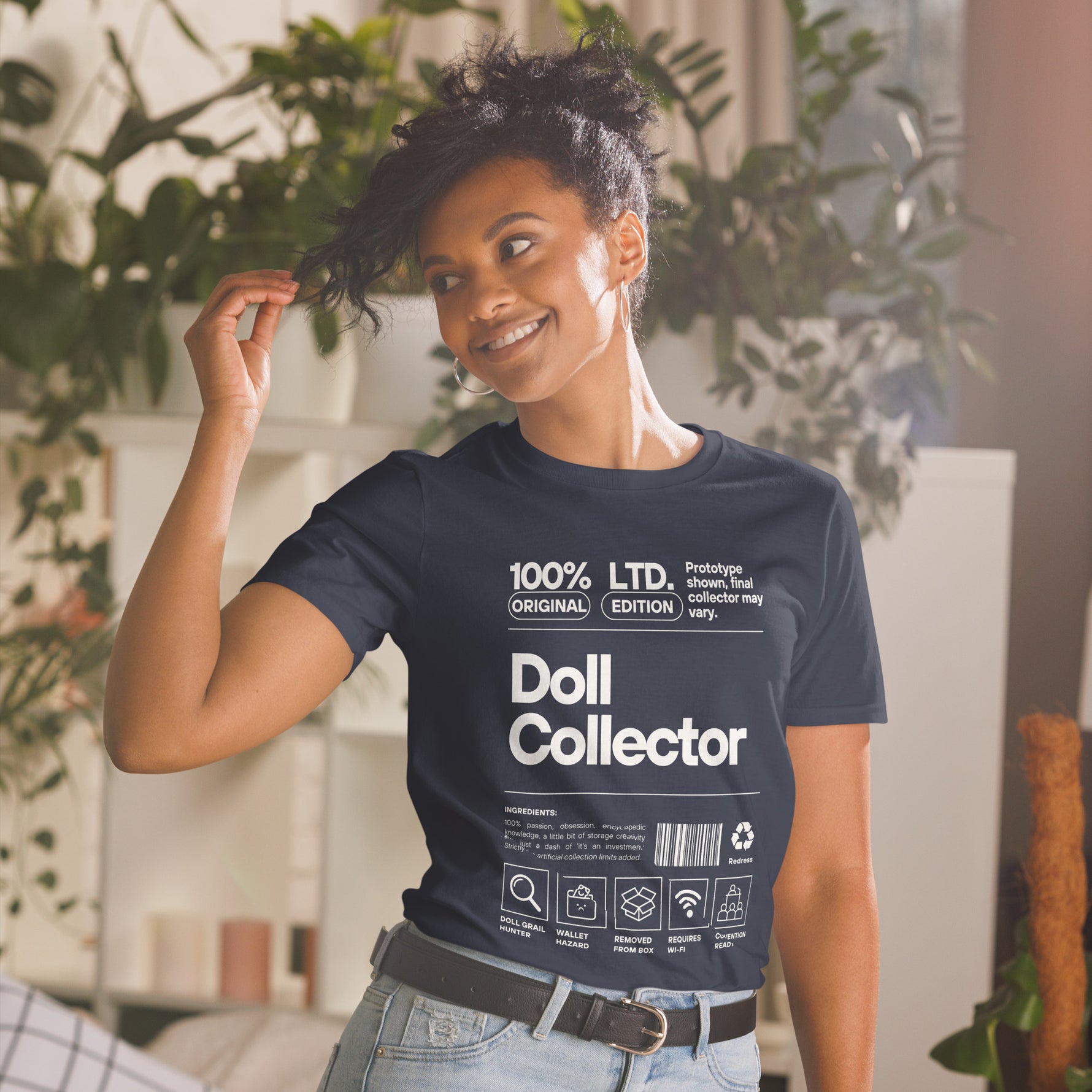 Person wearing a navy blue t-shirt with 'Doll Collector' text and graphics, standing indoors with plants in the background.