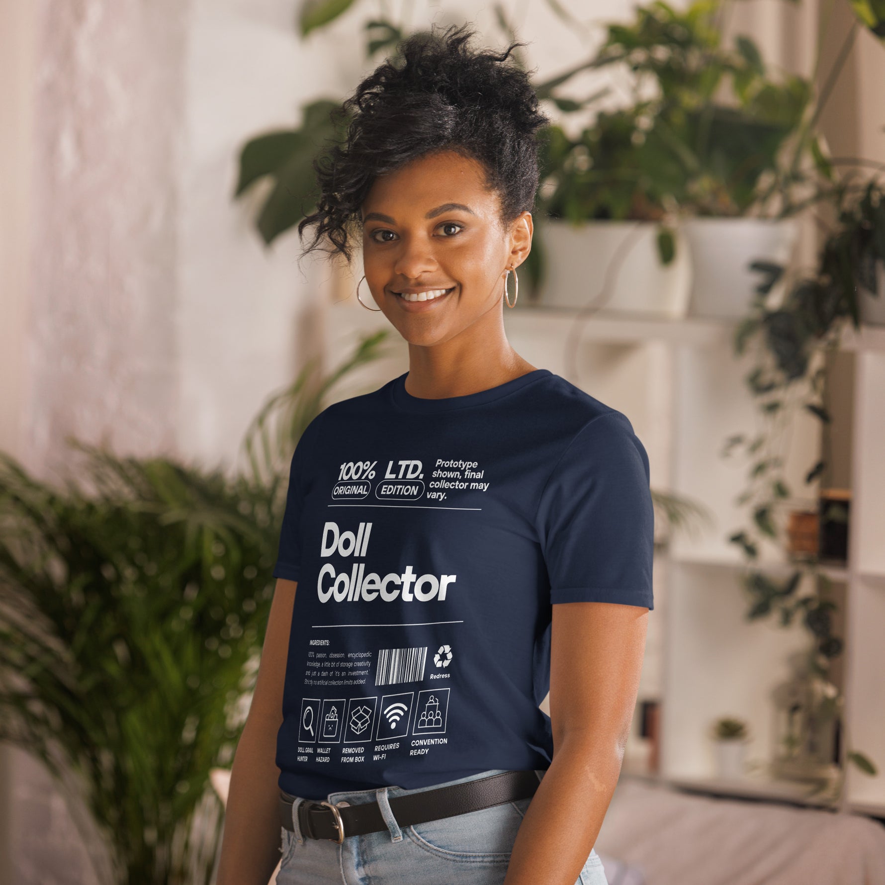 Person wearing a navy blue t-shirt with 'Doll Collector' text and graphics, standing in a casual setting with plants. 'Doll Collector' Product Label Design Short-Sleeve Unisex T-Shirt